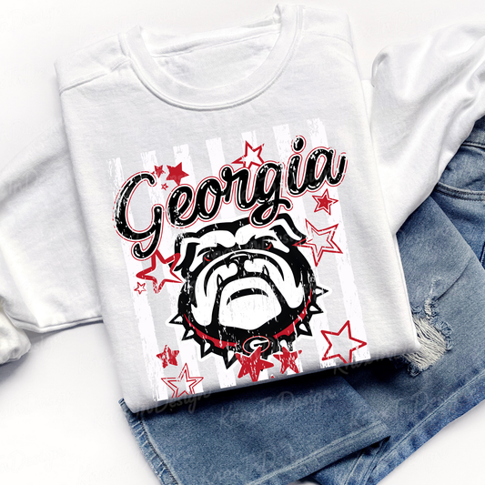 A folded white graphic T-shirt laid on top of blue denim shorts. The shirt features a distressed black-and-white bulldog illustration with red stars and the word 'Georgia' in black script across the front.