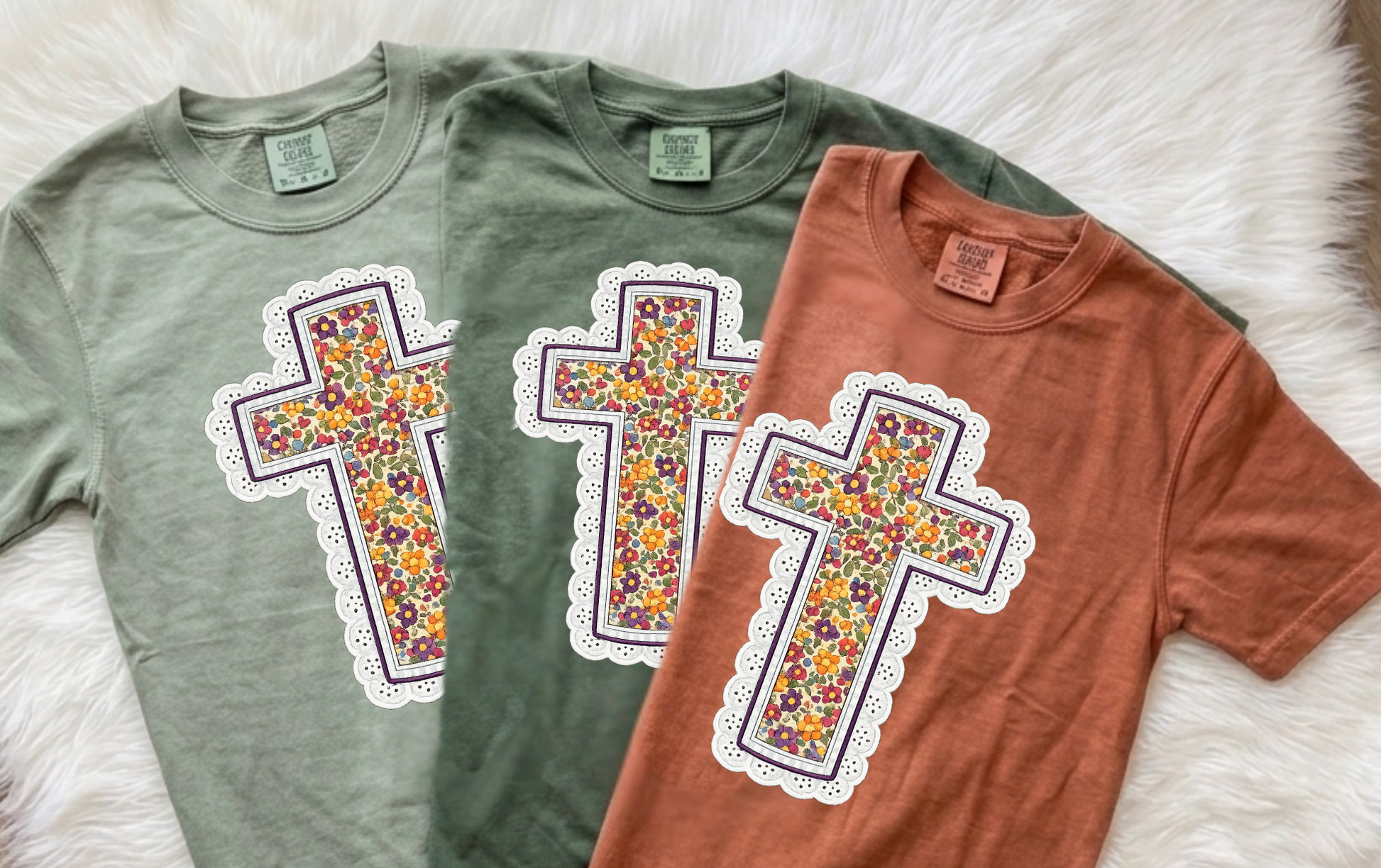 Two short-sleeve crewneck t-shirts laid flat on a white faux-fur surface. The shirt on the left is sage green, and the shirt on the right is terracotta orange.